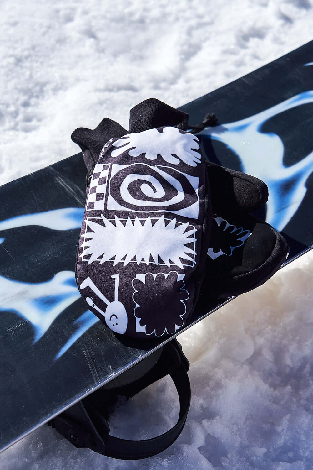 The KO Mitt x Glitterstudio Black mitten resting on a snowboard in the snow