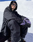 Snowboarder wearing The Team Transform x Glitterstudio Lavender mittens with Primaloft insulation, seated on a snowy slope.