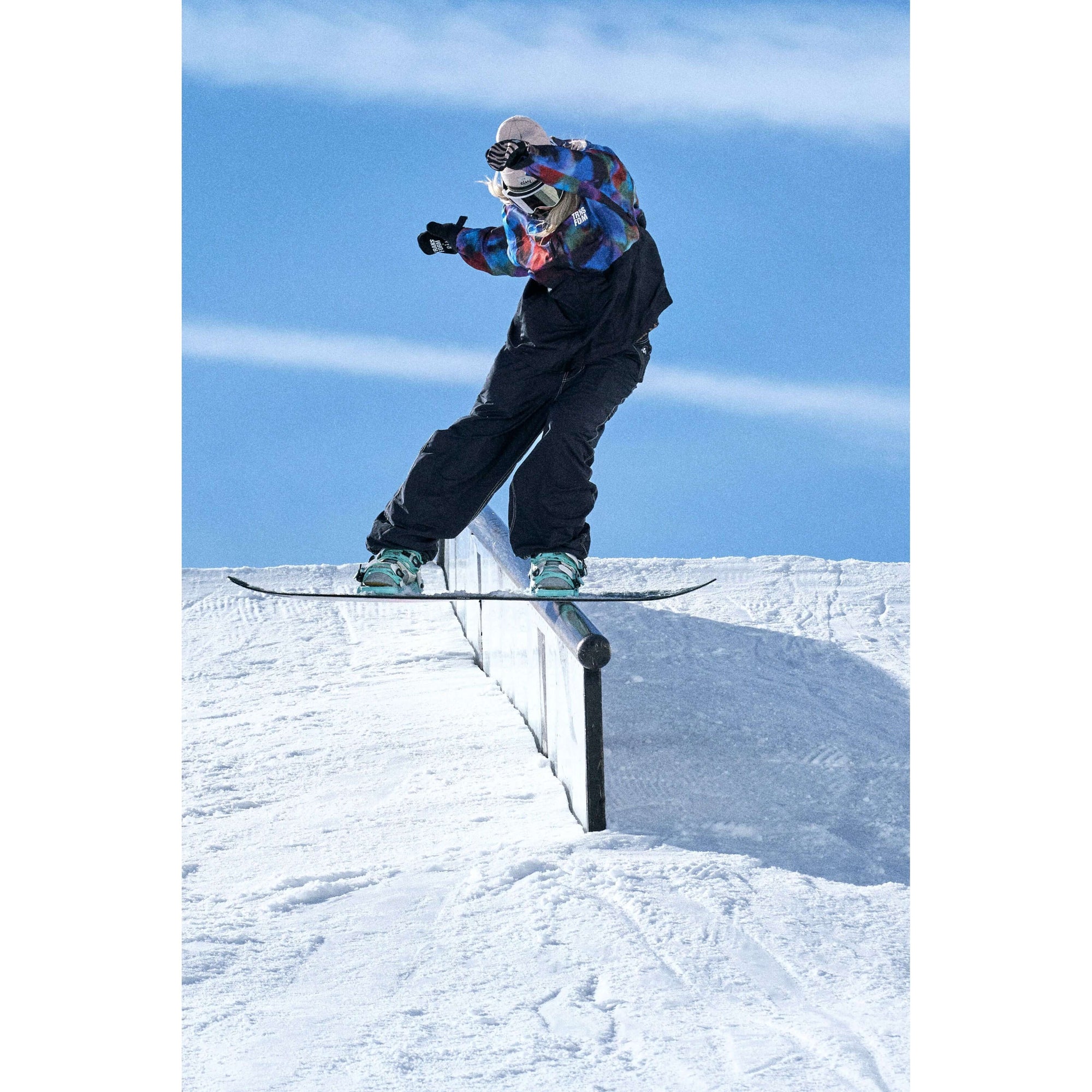 Snowboarder grinding rail in snow park wearing colorful jacket