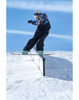 Snowboarder grinding rail in snow park wearing colorful jacket