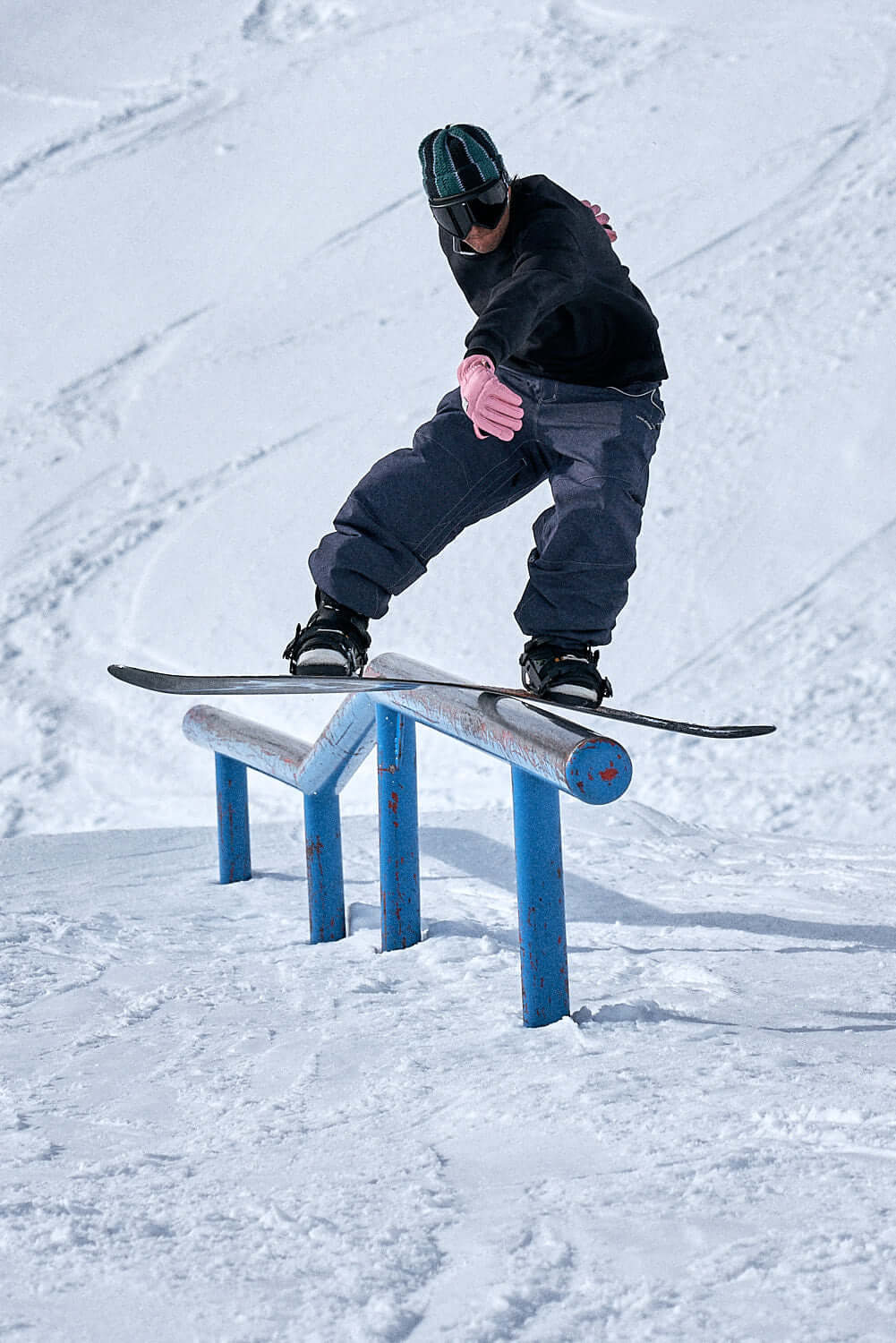 Snowboarder wearing pink gloves performing a rail slide trick on snowy terrain