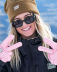 Woman smiling in winter gear with pink snowboarding gloves and brown hat enjoying snowy outdoors