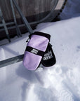 Pink and black snowboard mittens on snow with outdoor gear in the background.