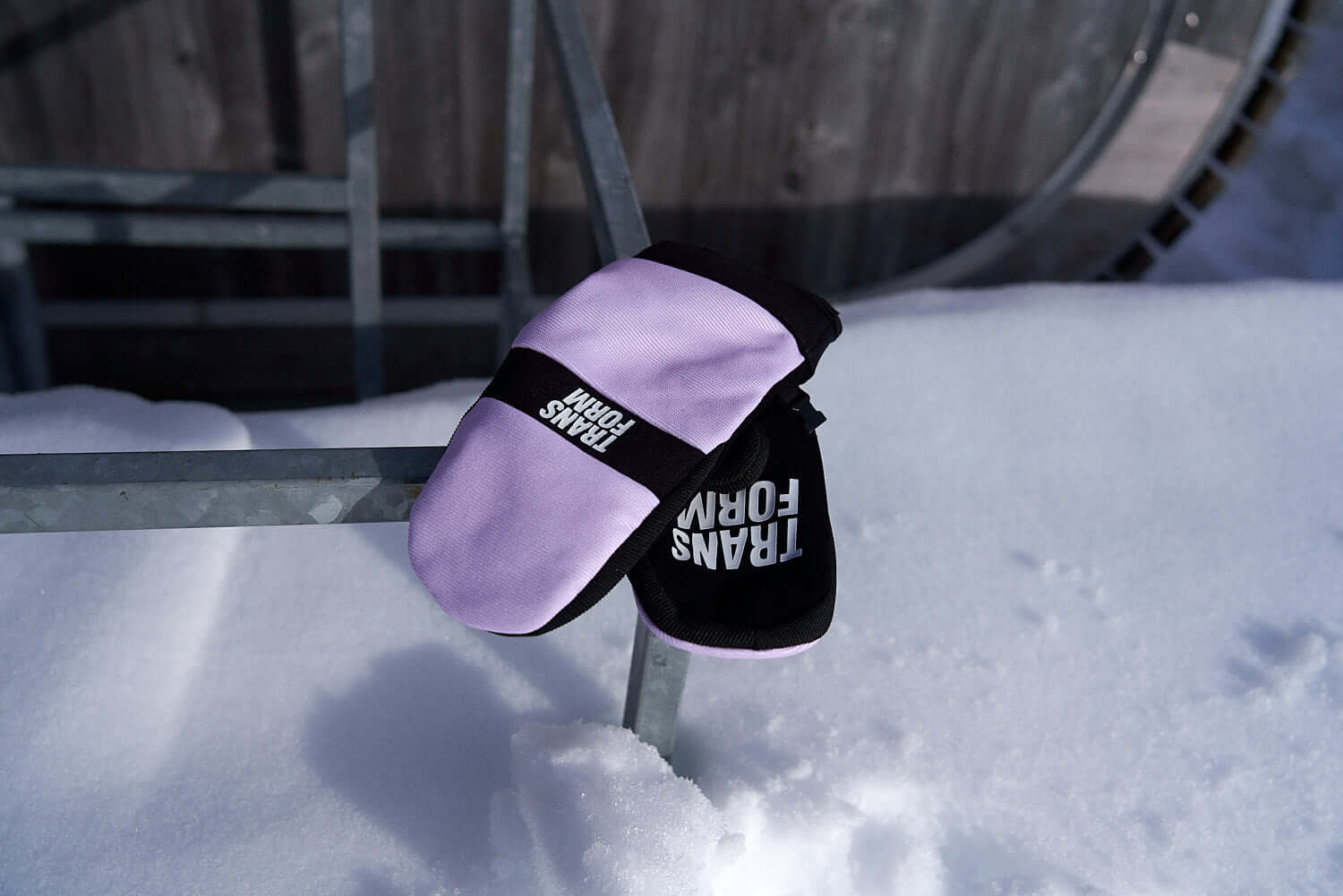 Pink and black snowboard mittens on snowy rail, perfect for spring snowboarding activities.