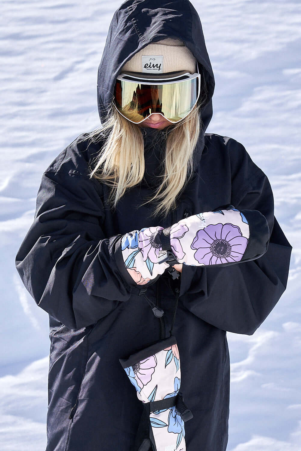 Person snowboarding in winter gear featuring The Team Transform x Eivy Big Flower mittens with Primaloft insulation and waterproof inserts.